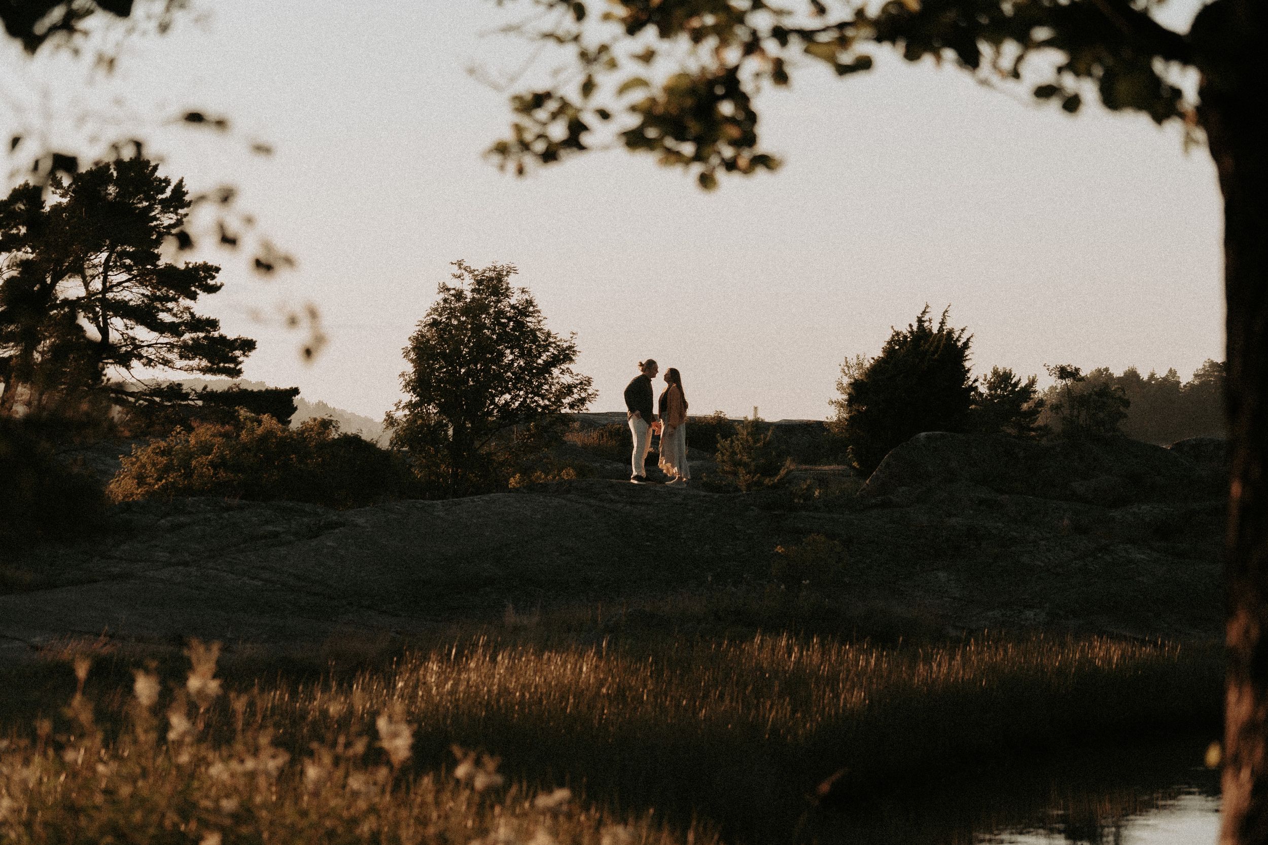 Silhouette of couple standing on hilltop during golden hour.