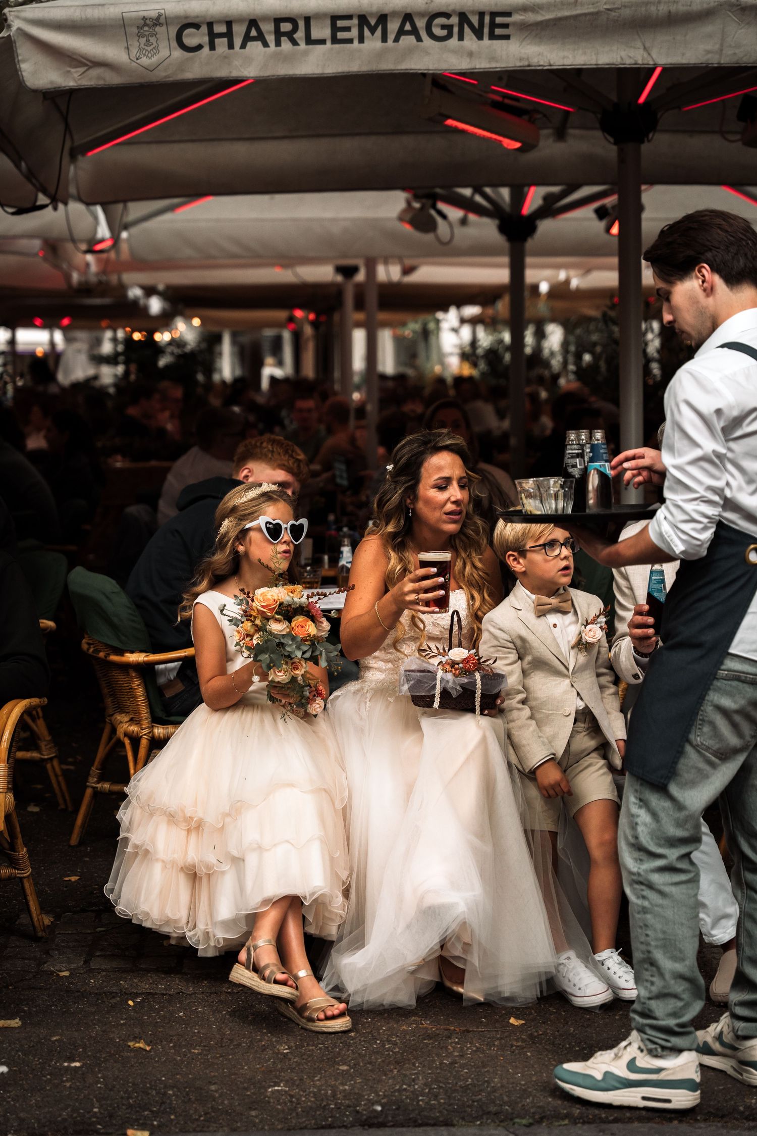 Young children in white dresses and formal attire sit at a restaurant table during what appears to be a special event.