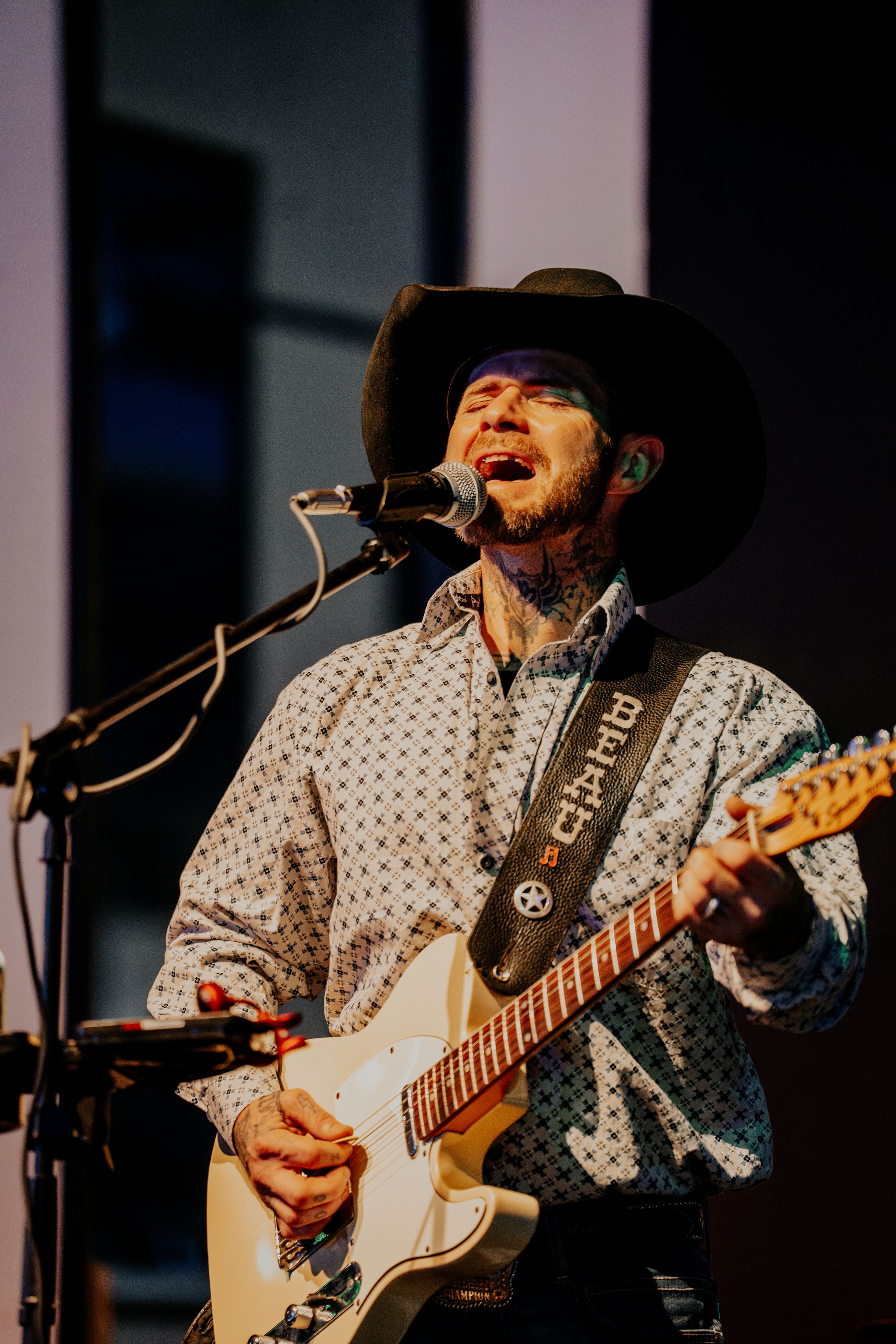 A country musician in a cowboy hat performs passionately with an electric guitar on stage.