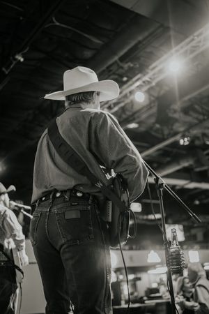 Black and white photo of a country musician performing on stage wearing a cowboy hat and jeans.
