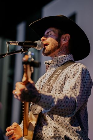 Close-up of country singer in cowboy hat and patterned shirt performing with microphone.