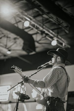 Black and white shot of musician singing and playing guitar under stage lighting.