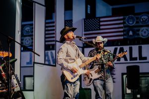 Country band members perform with guitars on stage with American flags and decorative backdrop.