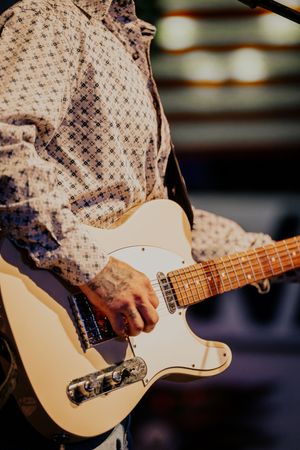 Close-up of white Telecaster guitar being played by musician in patterned shirt.