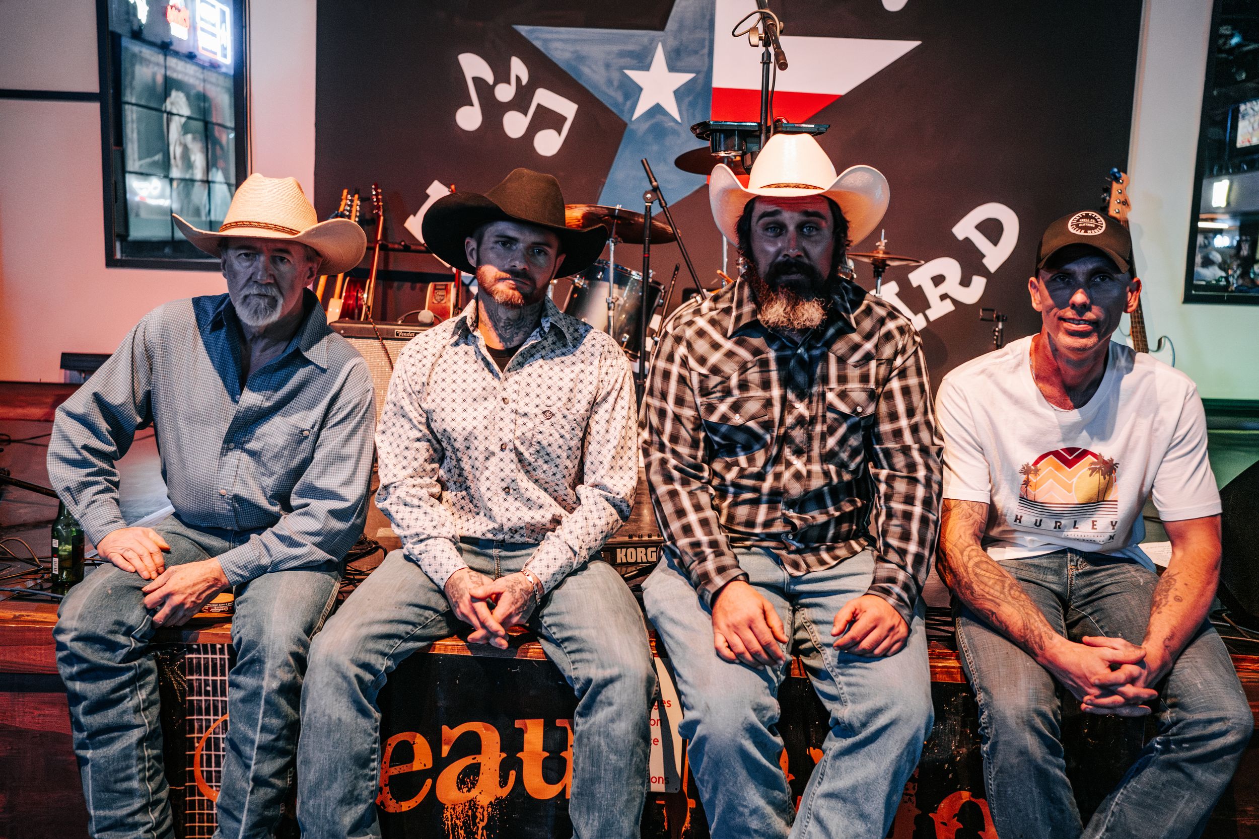 Country band members seated together in casual attire against musical note backdrop.