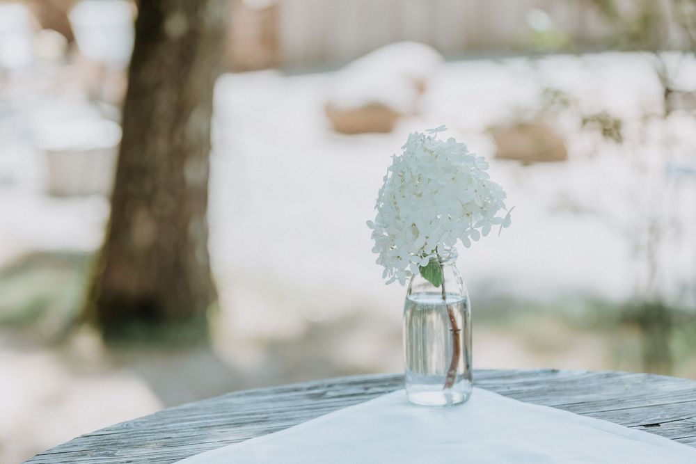 Delicate floral arrangements in glass vases create an elegant table setting at an outdoor wedding venue.