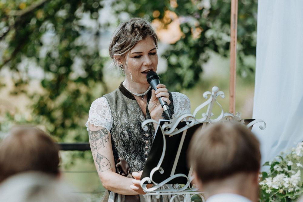 Outdoor wedding speeches taking place under decorative white banners and trees.