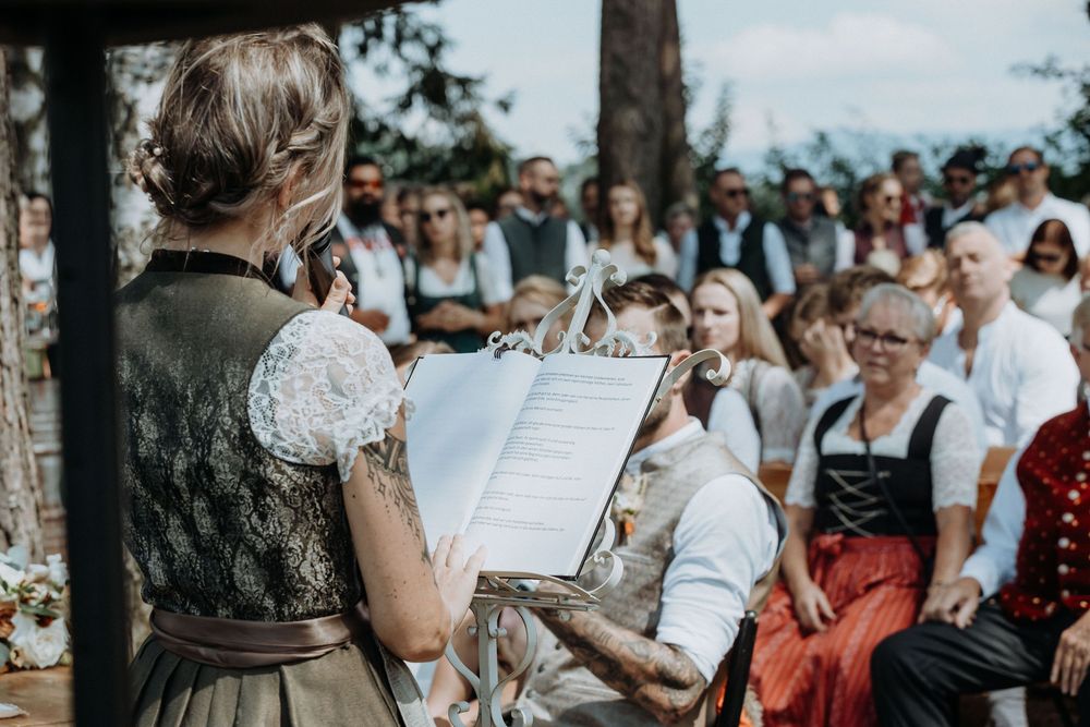 Wedding ceremony guests seated on wooden benches during an outdoor celebration.