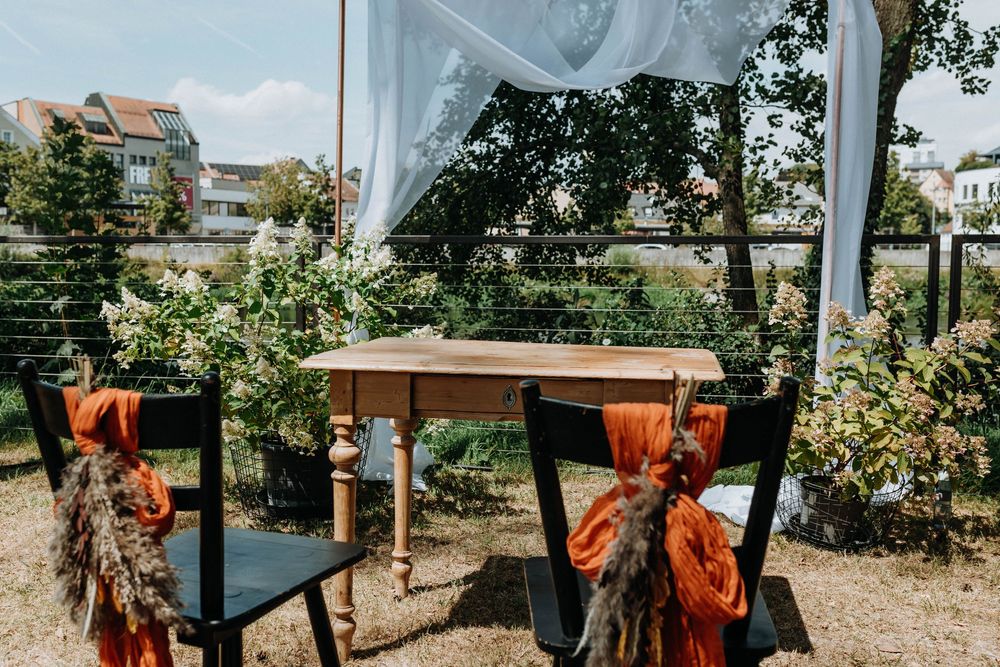 Orange floral decorations and wooden furniture set up for an outdoor wedding celebration.