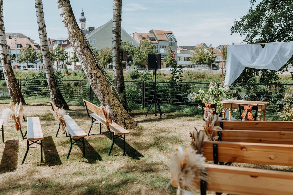 Rustic wooden benches arranged for an outdoor wedding ceremony with trees and houses in the background.