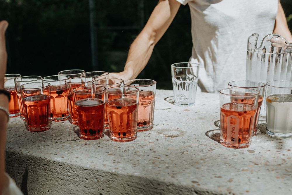 Orange-tinted cocktail glasses lined up on a table at an outdoor wedding reception.
