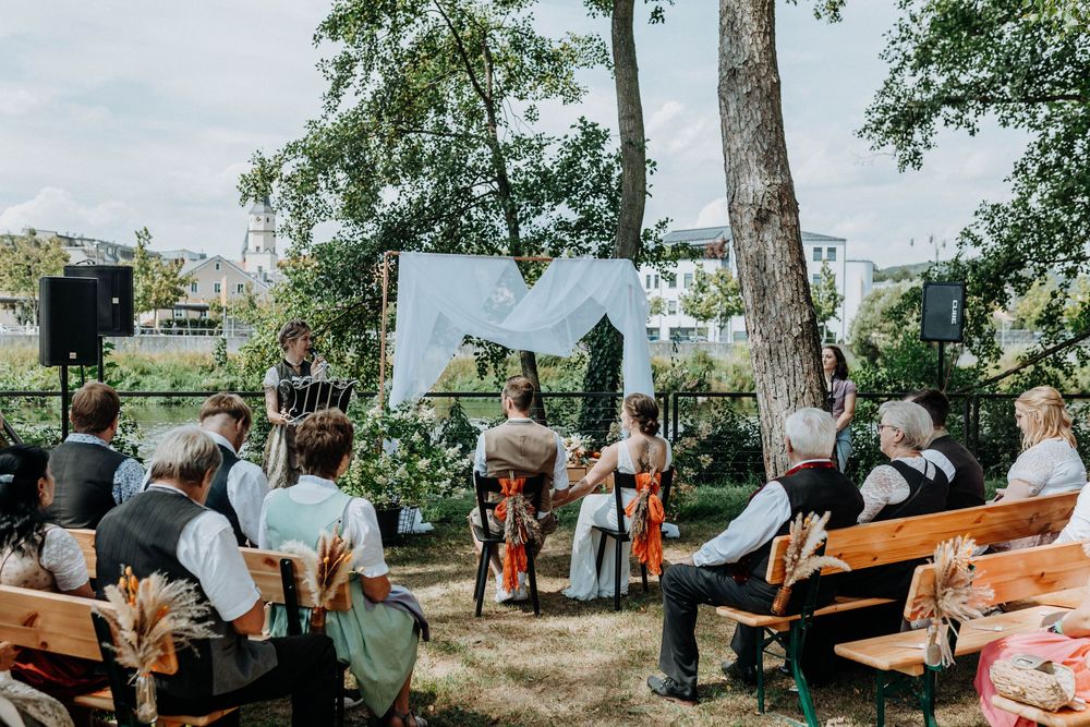 Wedding celebration in a park with string lights and decorations hanging between trees.