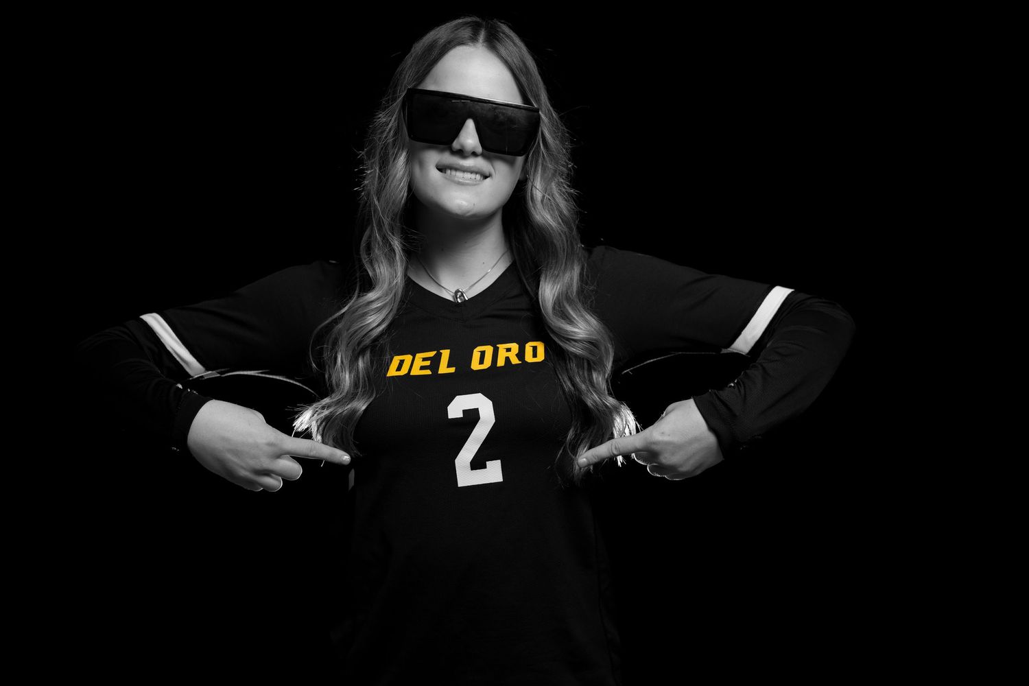 A person wearing a black sports jersey and sunglasses, posing in a dark setting.