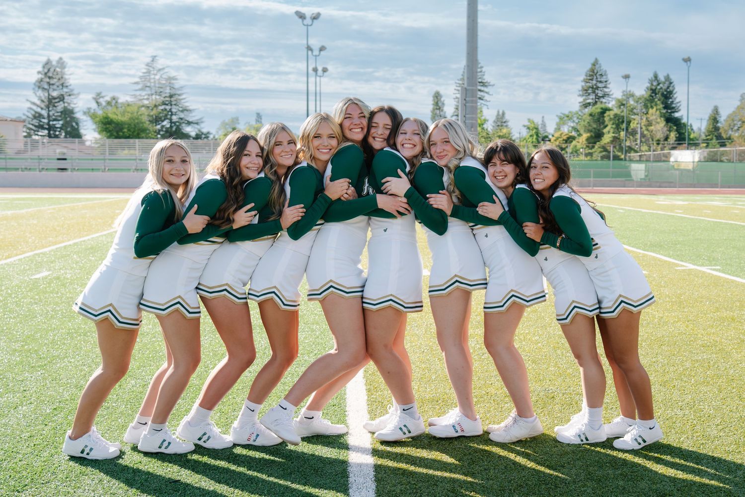 A group of cheerleaders in green and white uniforms pose together on a football field.