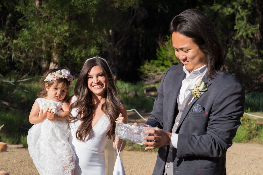 A group of wedding guests enjoying a sunny outdoor celebration in a natural setting.