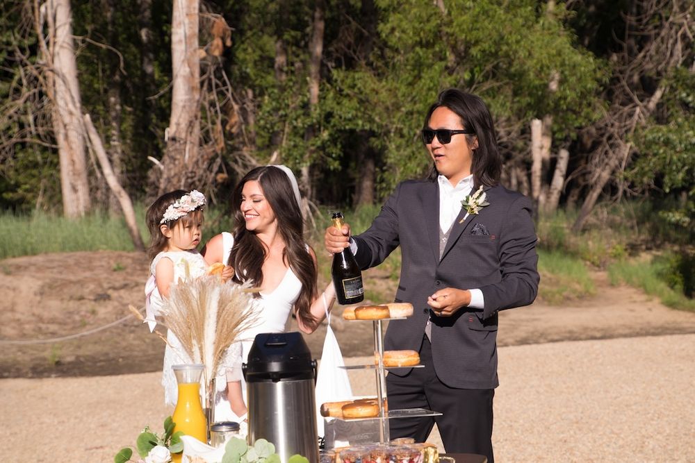 A couple celebrates their outdoor wedding ceremony with champagne toasts at a rustic venue surrounded by trees.