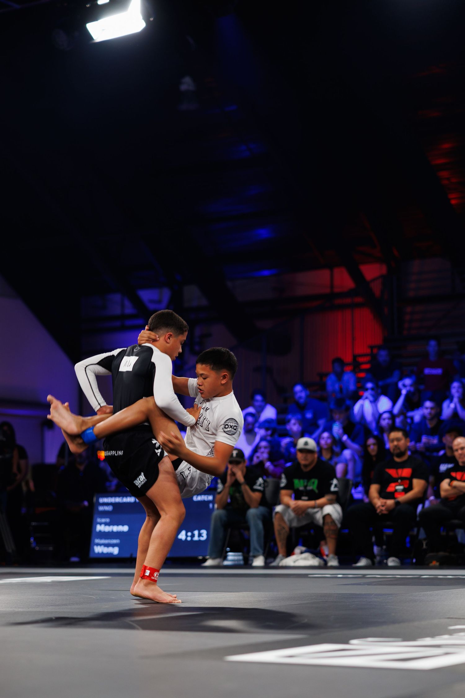 Two competitors in martial arts match executing takedown moves on competition mat.