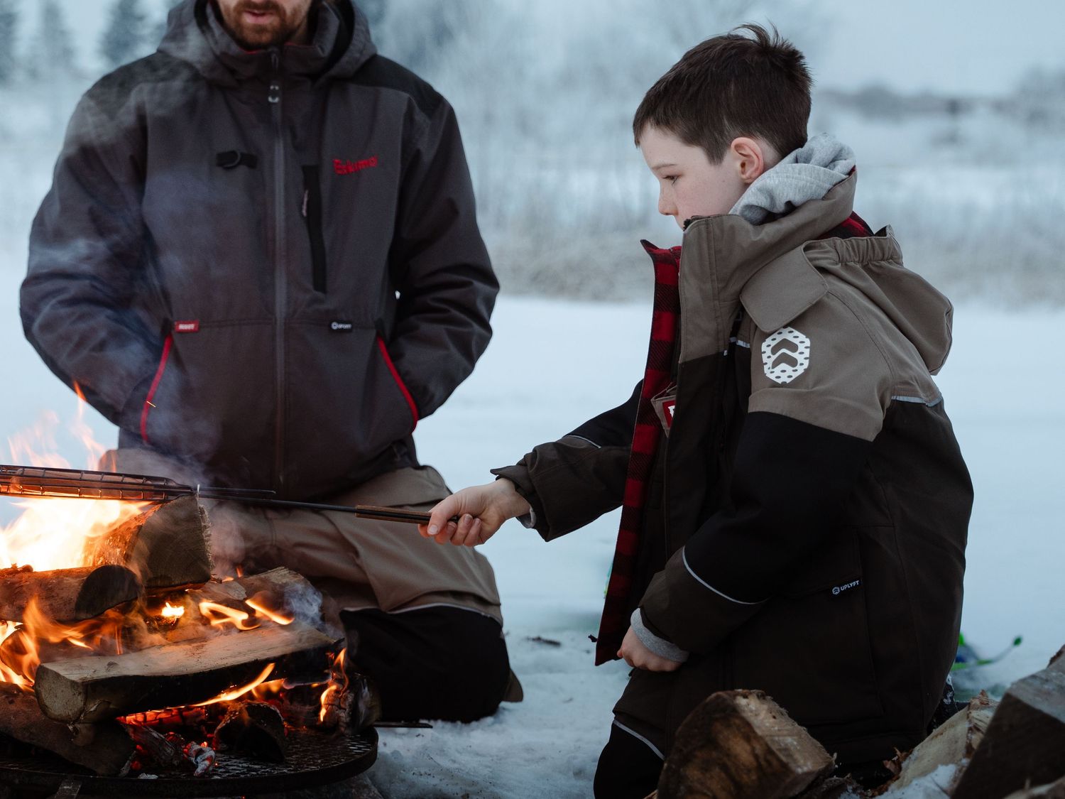 People warming up by campfire while ice fishing on winter day.