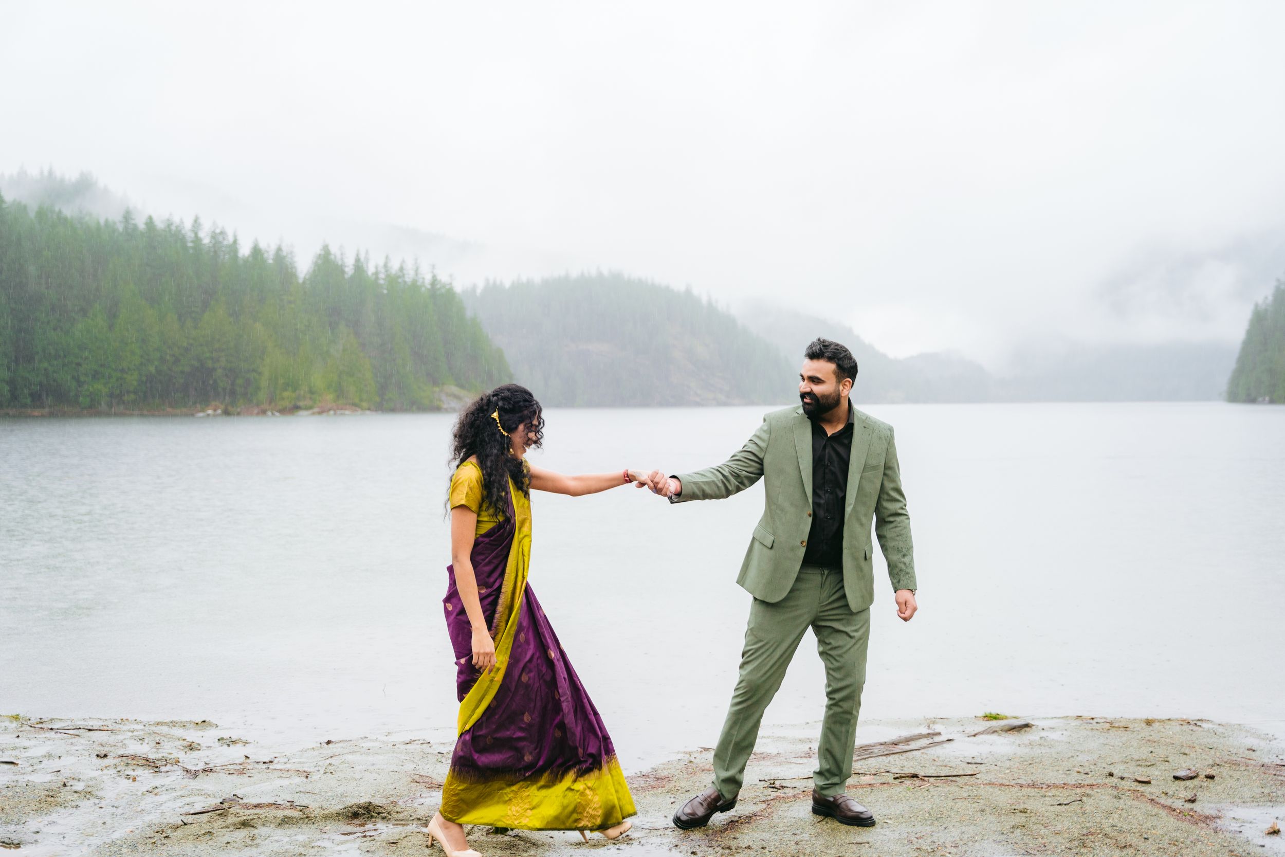 A couple stands on a misty beach shore in coordinated outfits during a romantic photoshoot.