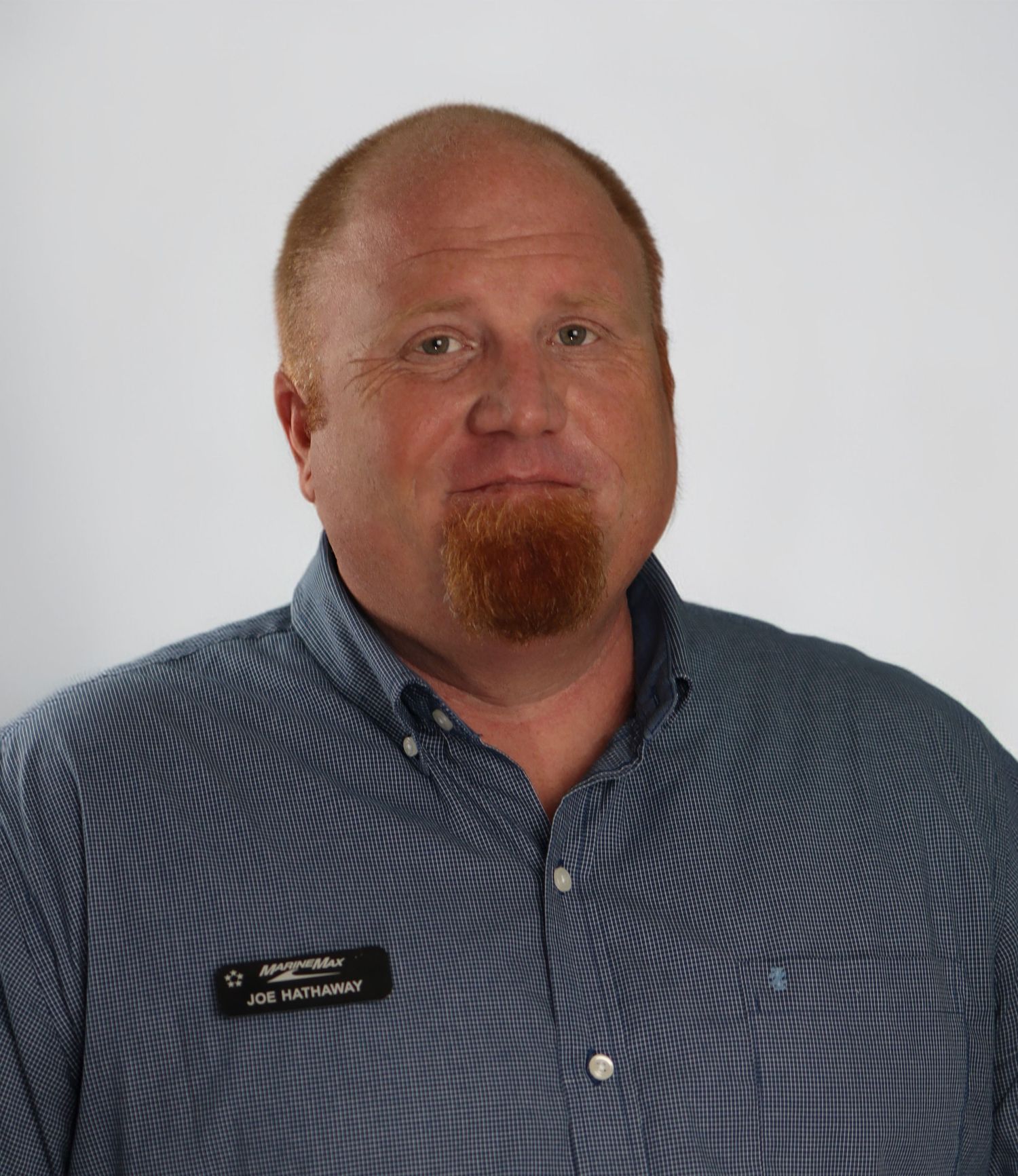 A person wearing a blue collared shirt with a red beard looks at the camera with a marina visible in the background.