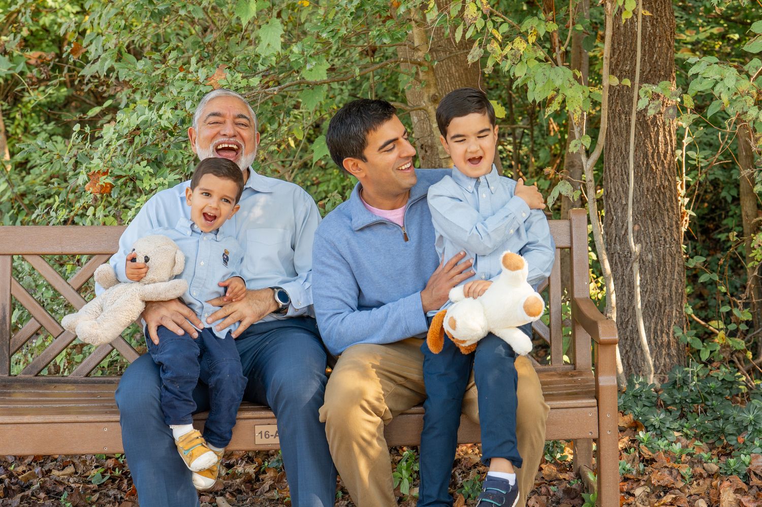 A family sits together on a wooden bench in a garden while sharing laughs during a family photo session in Northern Virginia.