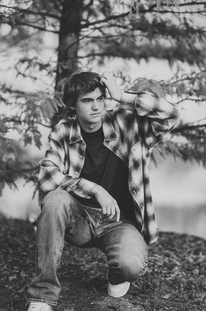 Casual portrait in plaid flannel shirt and jeans against forest backdrop in black and white style.