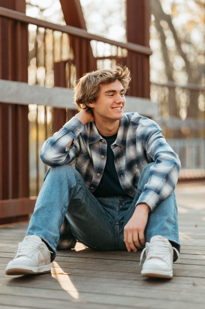 Person relaxes on wooden deck wearing plaid flannel and denim in golden hour lighting.