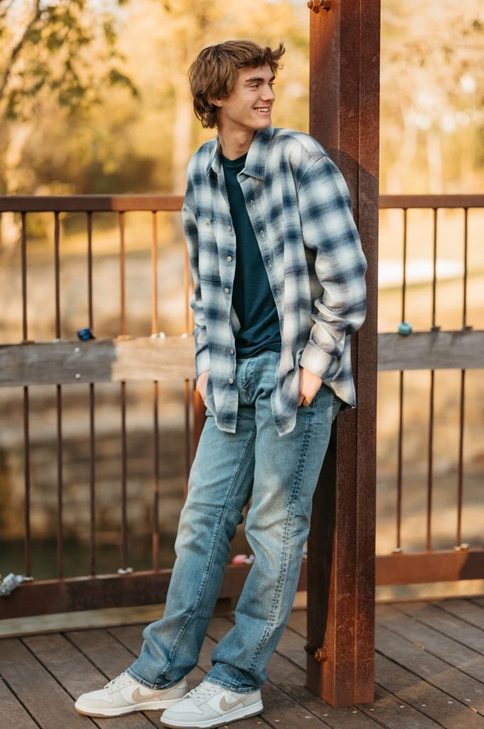Casual portrait of someone in a blue plaid flannel shirt and jeans standing on a wooden deck at sunset.