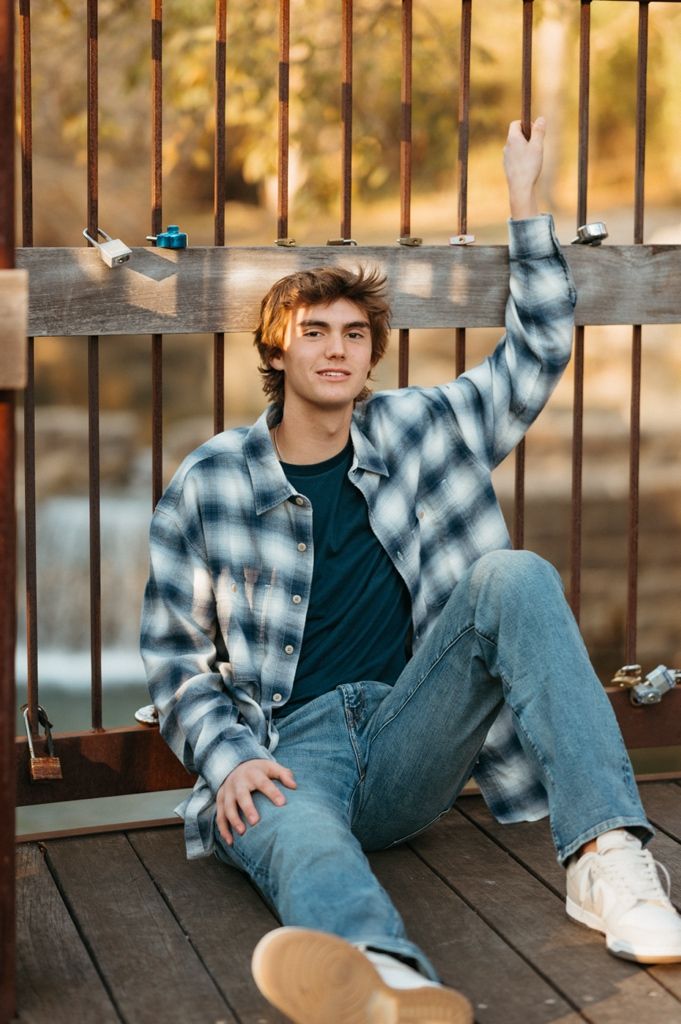 Relaxed pose on wooden deck wearing plaid flannel and jeans in warm autumn lighting.