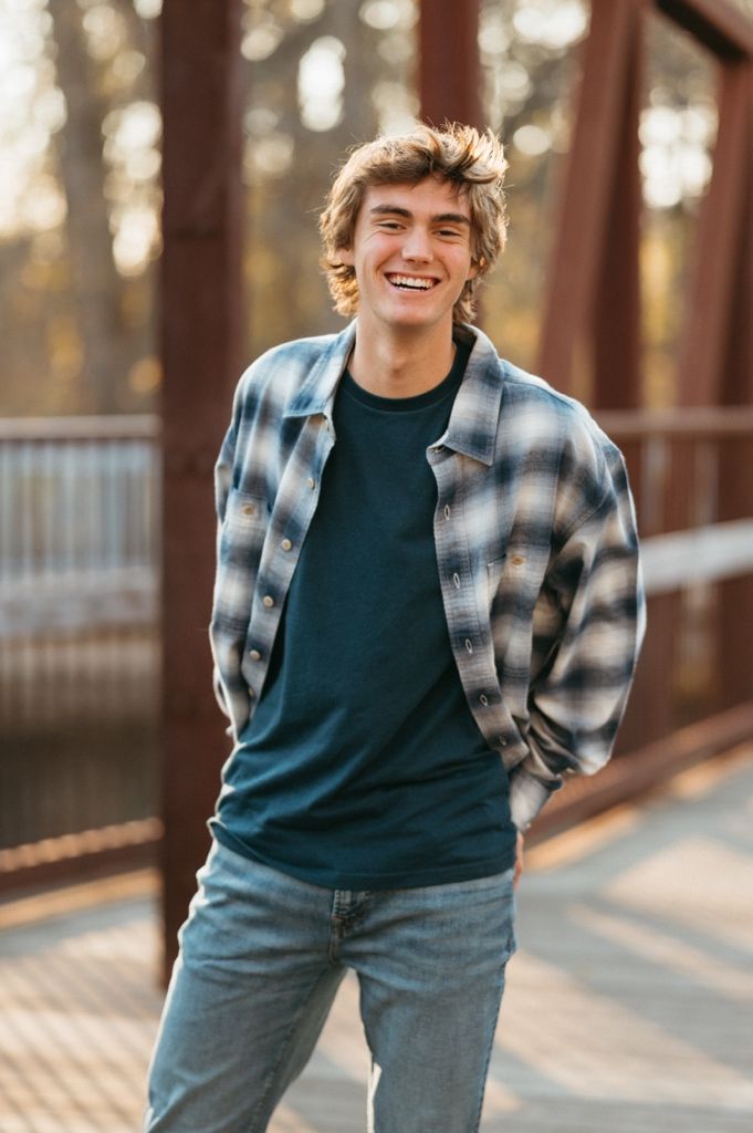 A casual outdoor portrait showing someone wearing a plaid flannel shirt and dark t-shirt in warm sunlight.