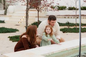 People lean over a low wall to look at something in a garden or water feature on a sunny day.