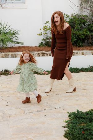 Two people in coordinating outfits dance joyfully on a stone patio, one wearing a brown dress and one in mint green.