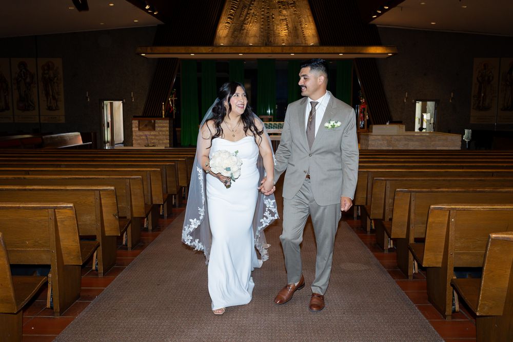 Bride and groom walk hand in hand down church aisle after wedding ceremony.