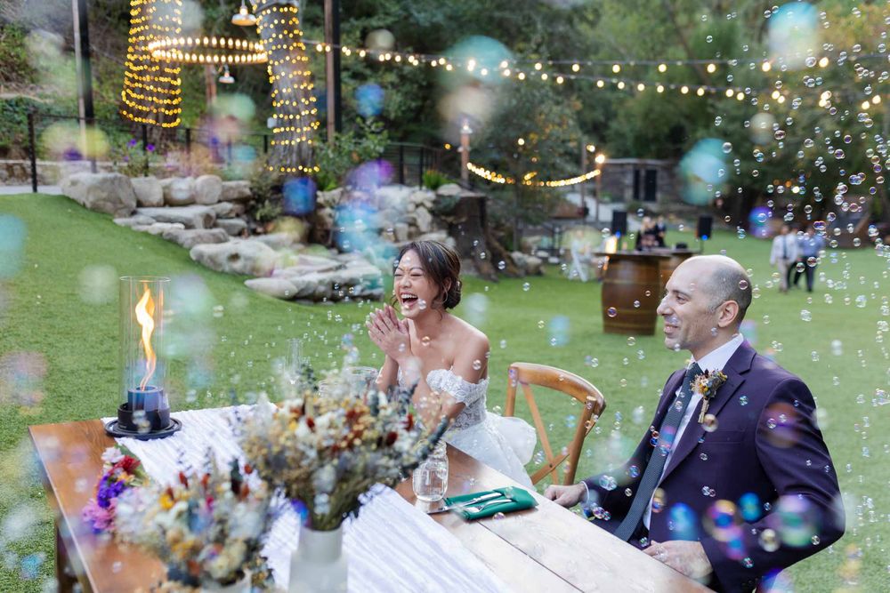 Wedding reception celebration outdoors with string lights and bubbles creating a magical evening atmosphere.