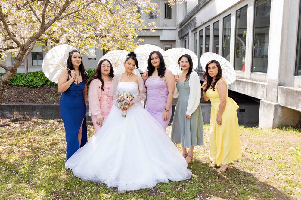 Wedding party poses outdoors in pastel yellow and pink bridesmaid dresses among fall foliage.