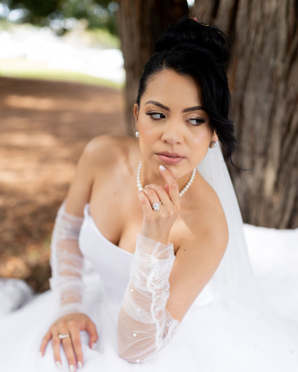 Close-up portrait shots of a bride in a white wedding dress wearing pearl jewelry and showing off her ring.
