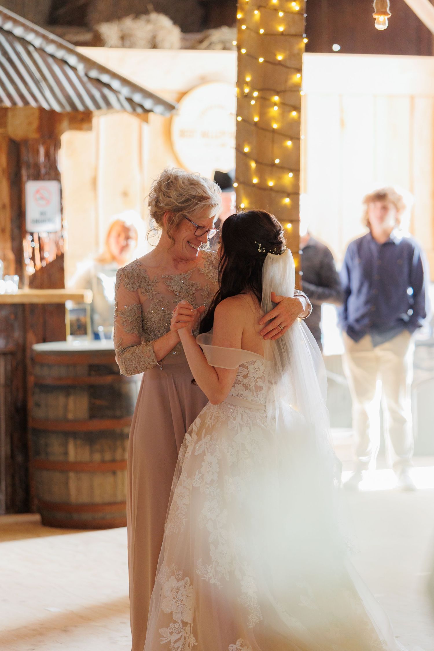 Emotional candid moment shared between a mother and the bride during a dance at a wedding in a rustic barn venue.