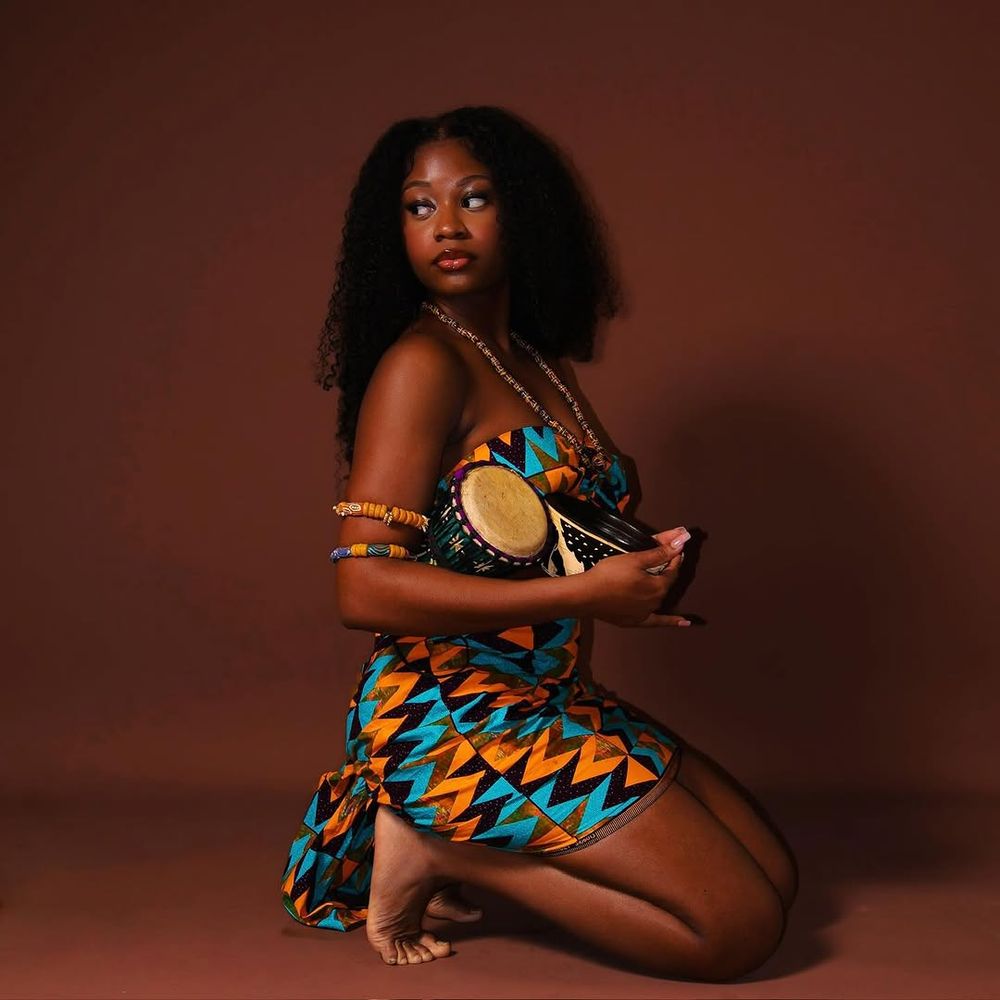 Artistic photo series showing a woman in traditional African print fabric posing gracefully against a dark brown backdrop.