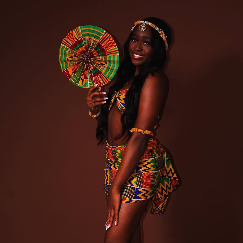 Traditional African-inspired fashion with colorful kente print fan and matching outfit against dark brown background.