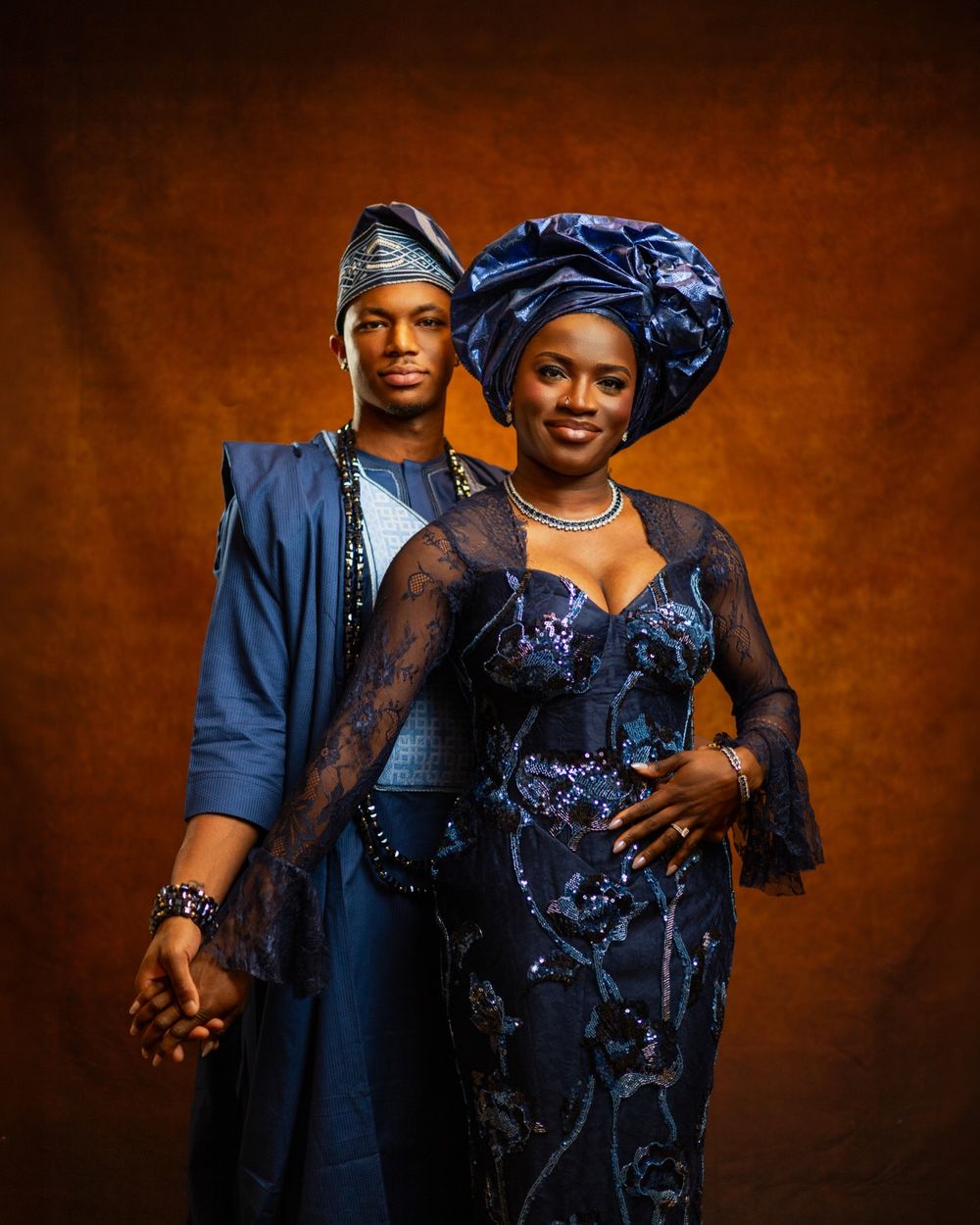 Couple in matching blue Nigerian traditional attire, gele headwrap and agbada, posing for a portrait.