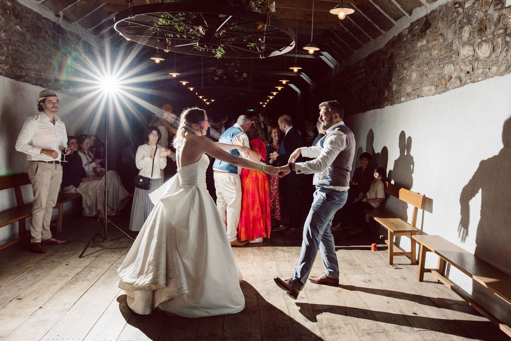 Couples dancing together in a rustic barn venue with dramatic lighting during a wedding reception celebration.