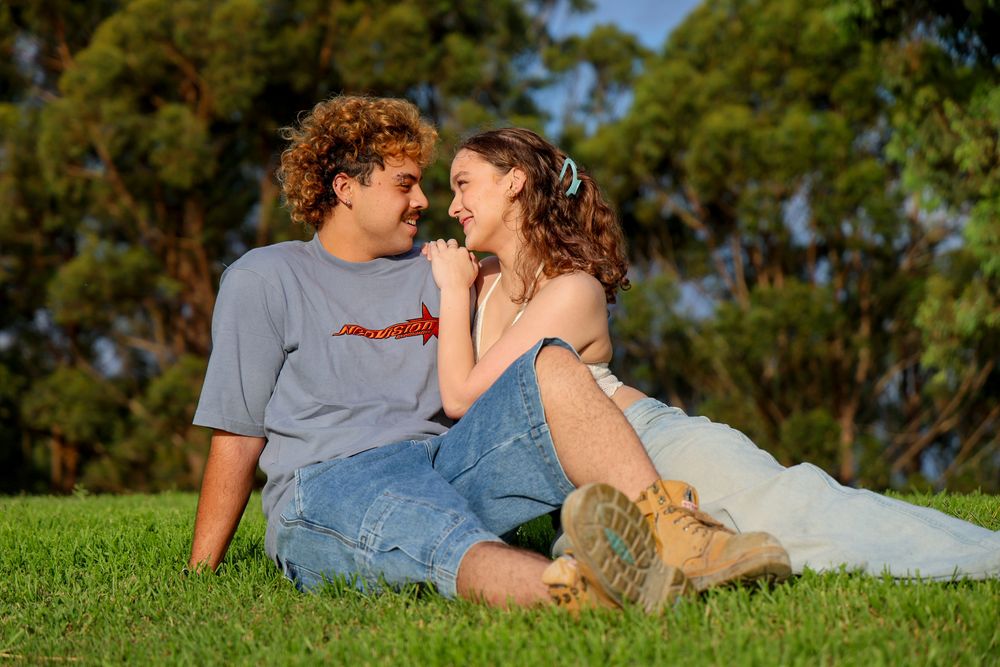 A young couple sitting in the sun together while cuddling slightly