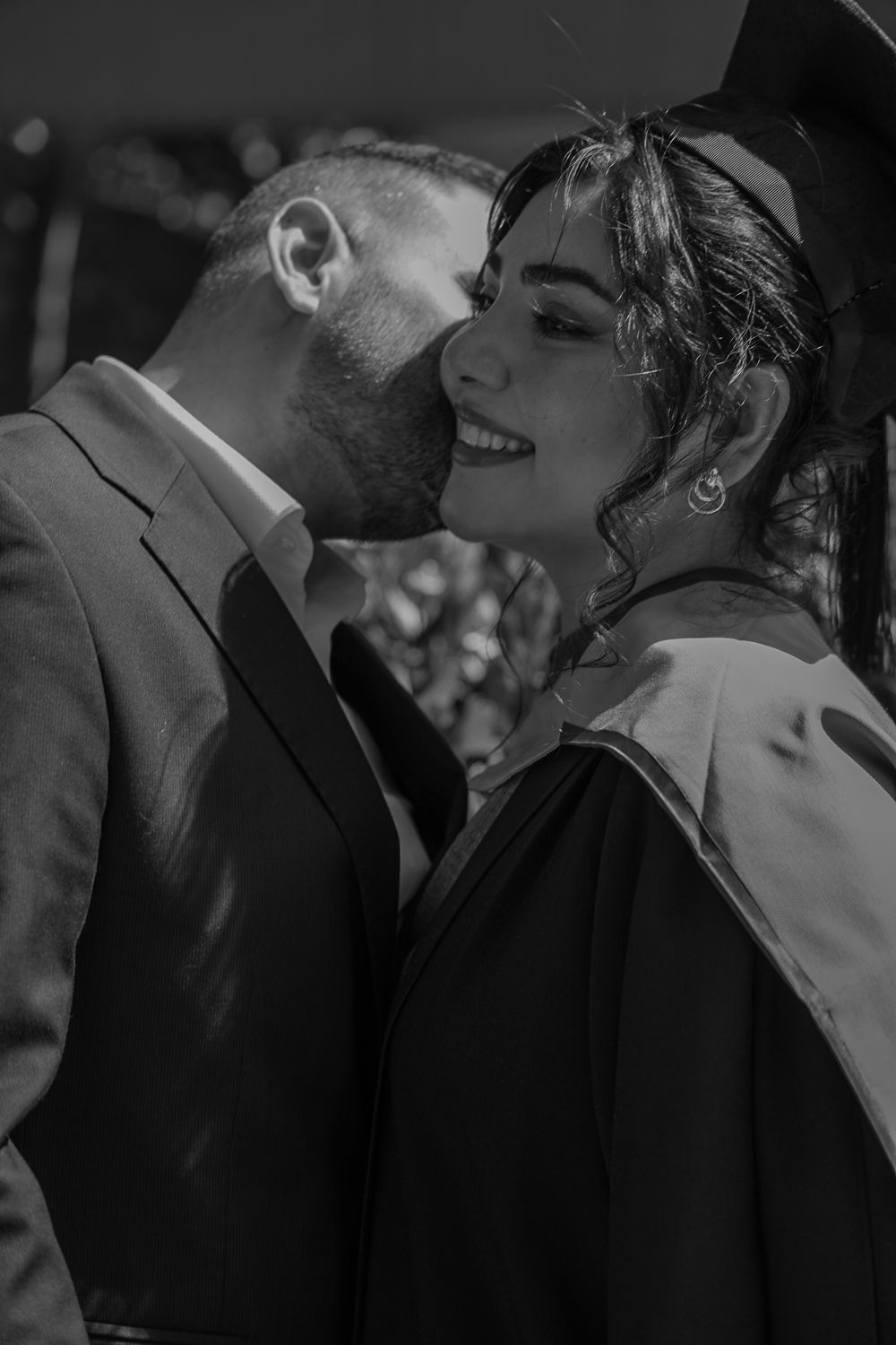 A woman graduating from university and her partner kissing her on the cheek