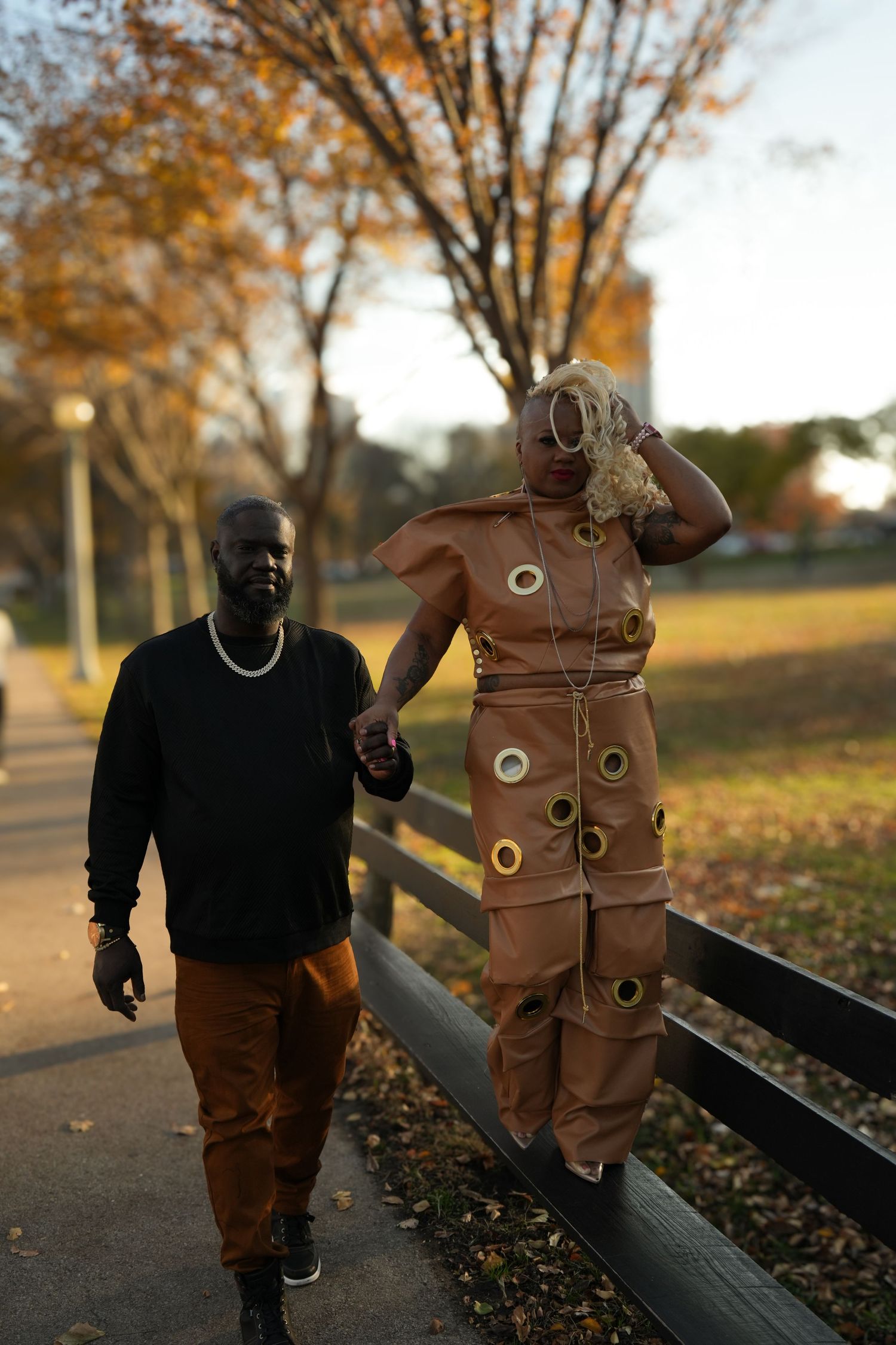 Two figures in autumn attire walking along a park bench surrounded by fallen leaves at sunset | Sydney Allen Photography