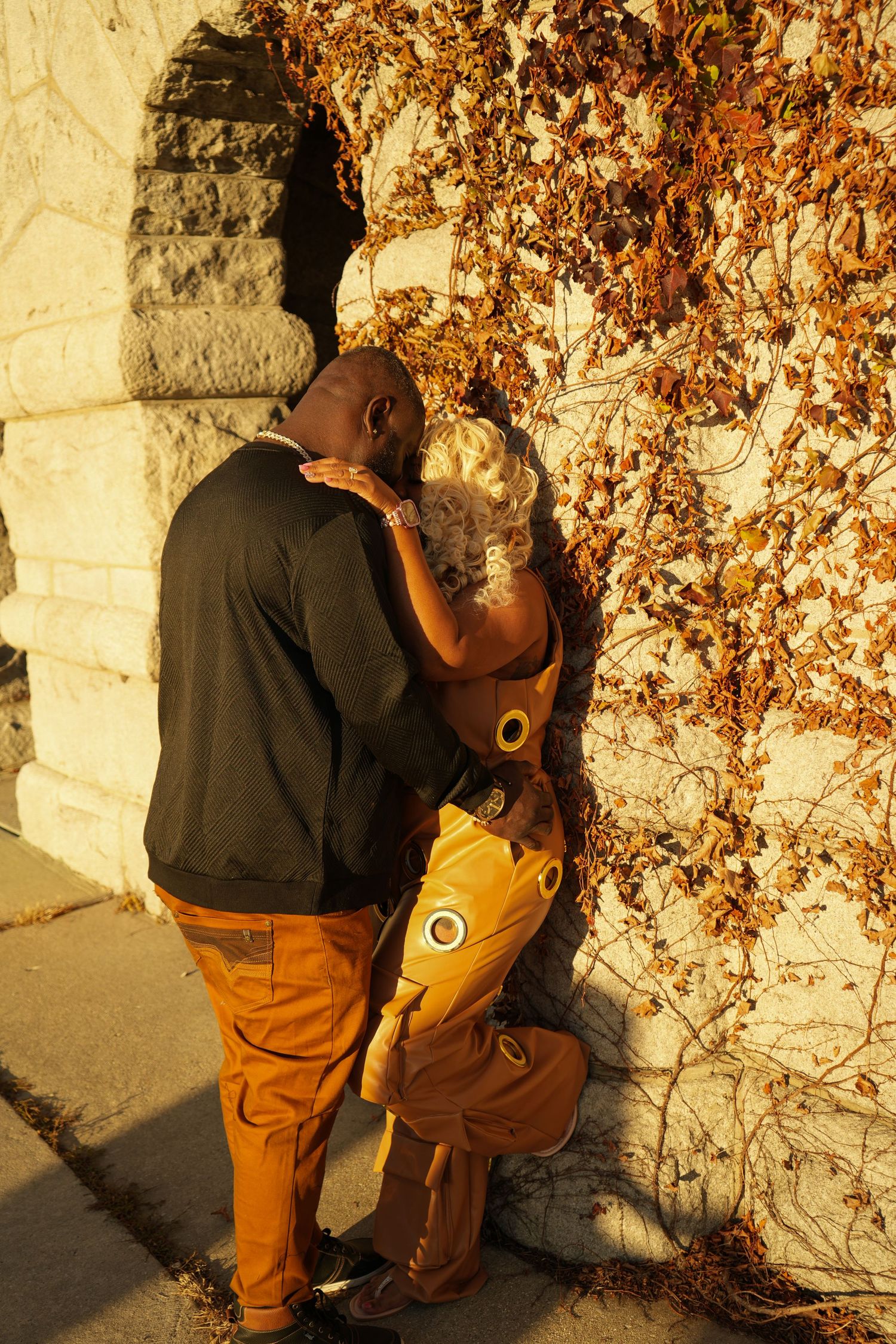 A couple embraces against a stone wall with autumn vines during golden hour sunlight | Sydney Allen Photography