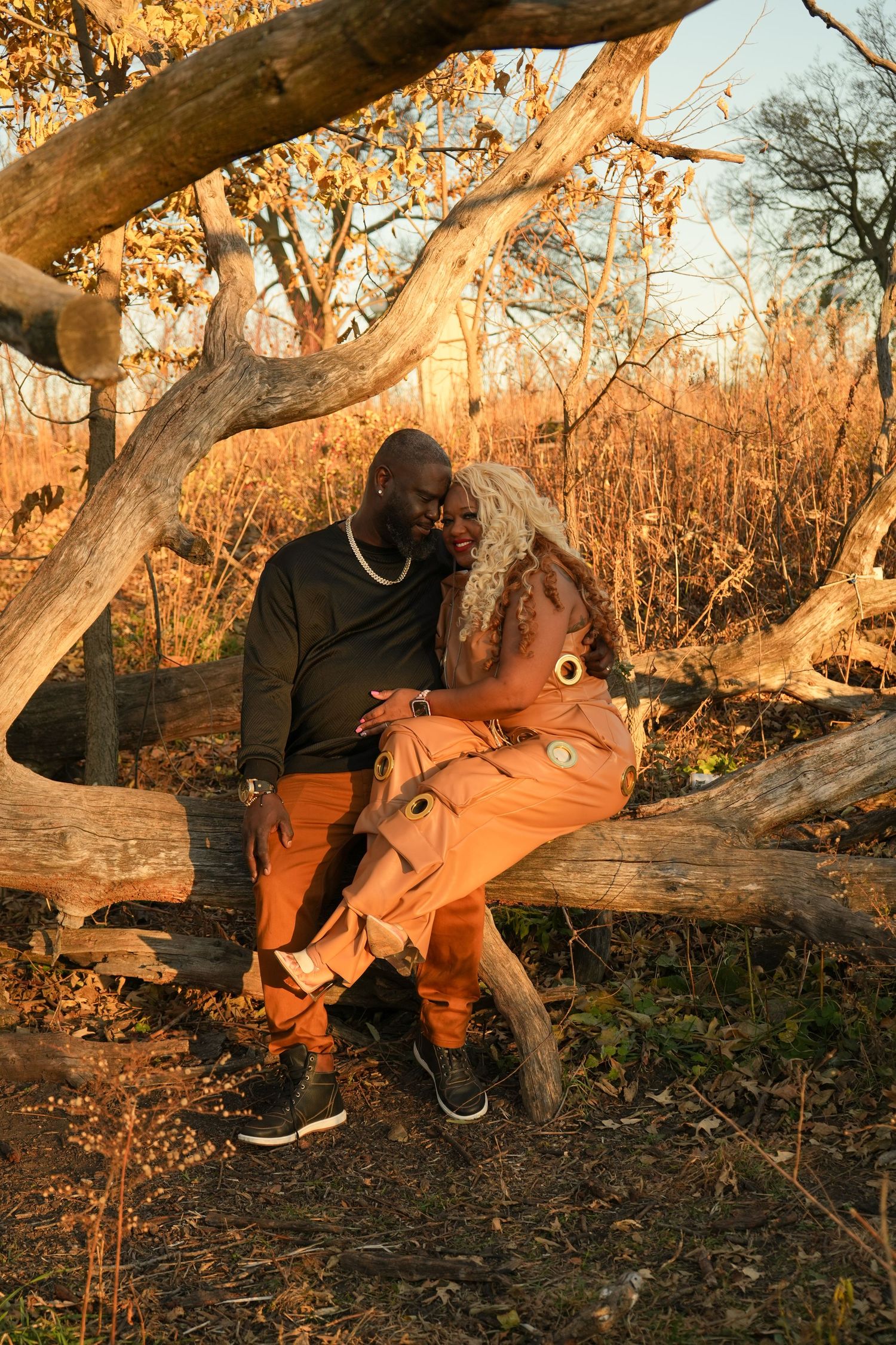 Two people in casual clothing exploring a fallen tree branch in a golden-lit autumn forest setting | Sydney Allen Photography