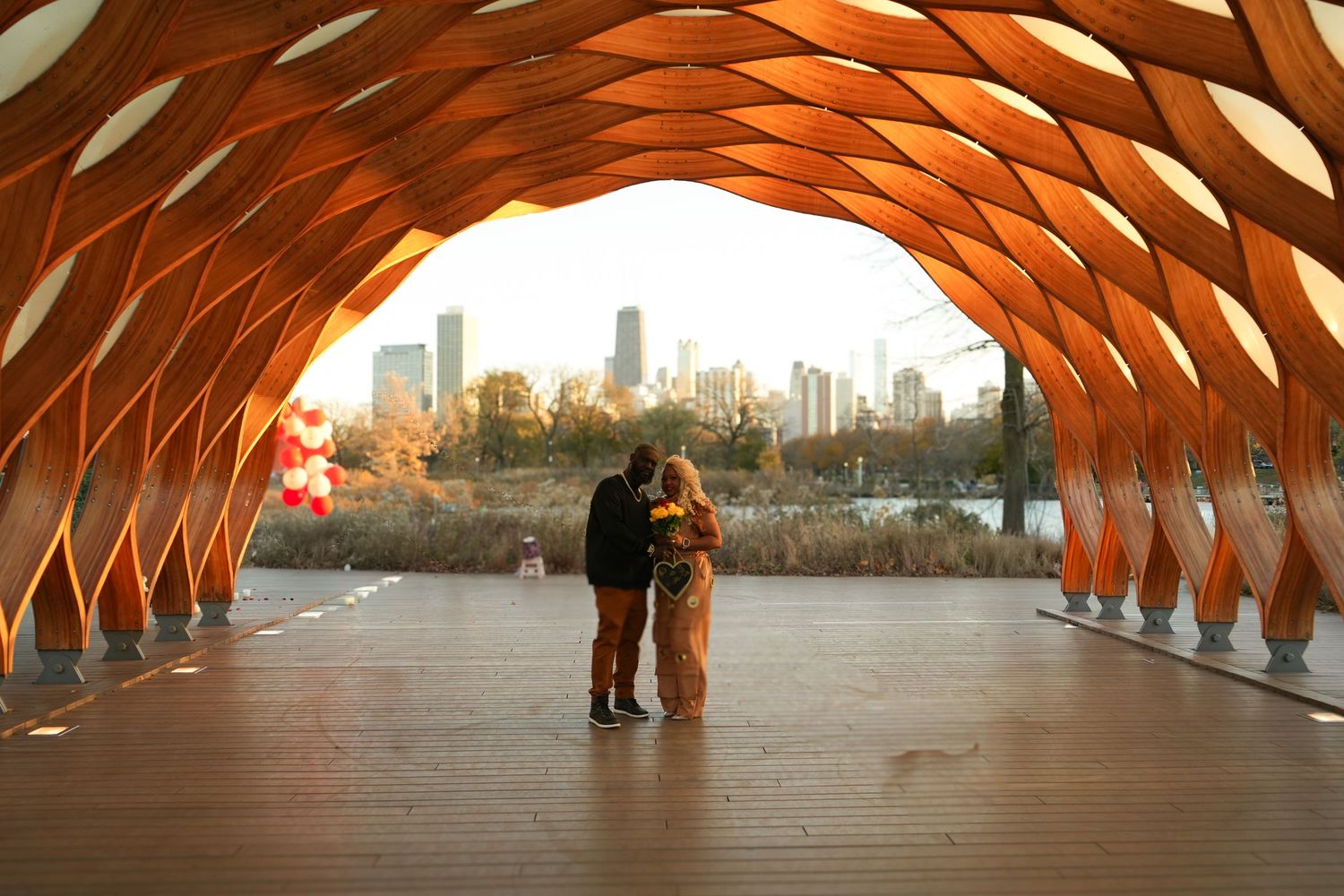 A couple stands silhouetted inside a wooden tunnel structure with city skyline visible in background | Sydney Allen Photography