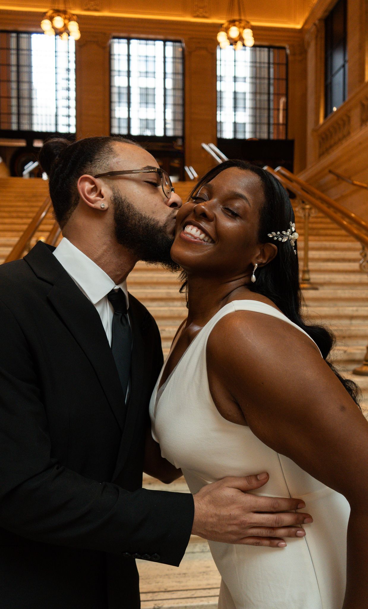 A groom in a black suit kisses his smiling bride in a white gown at Grand Central Terminal wedding.