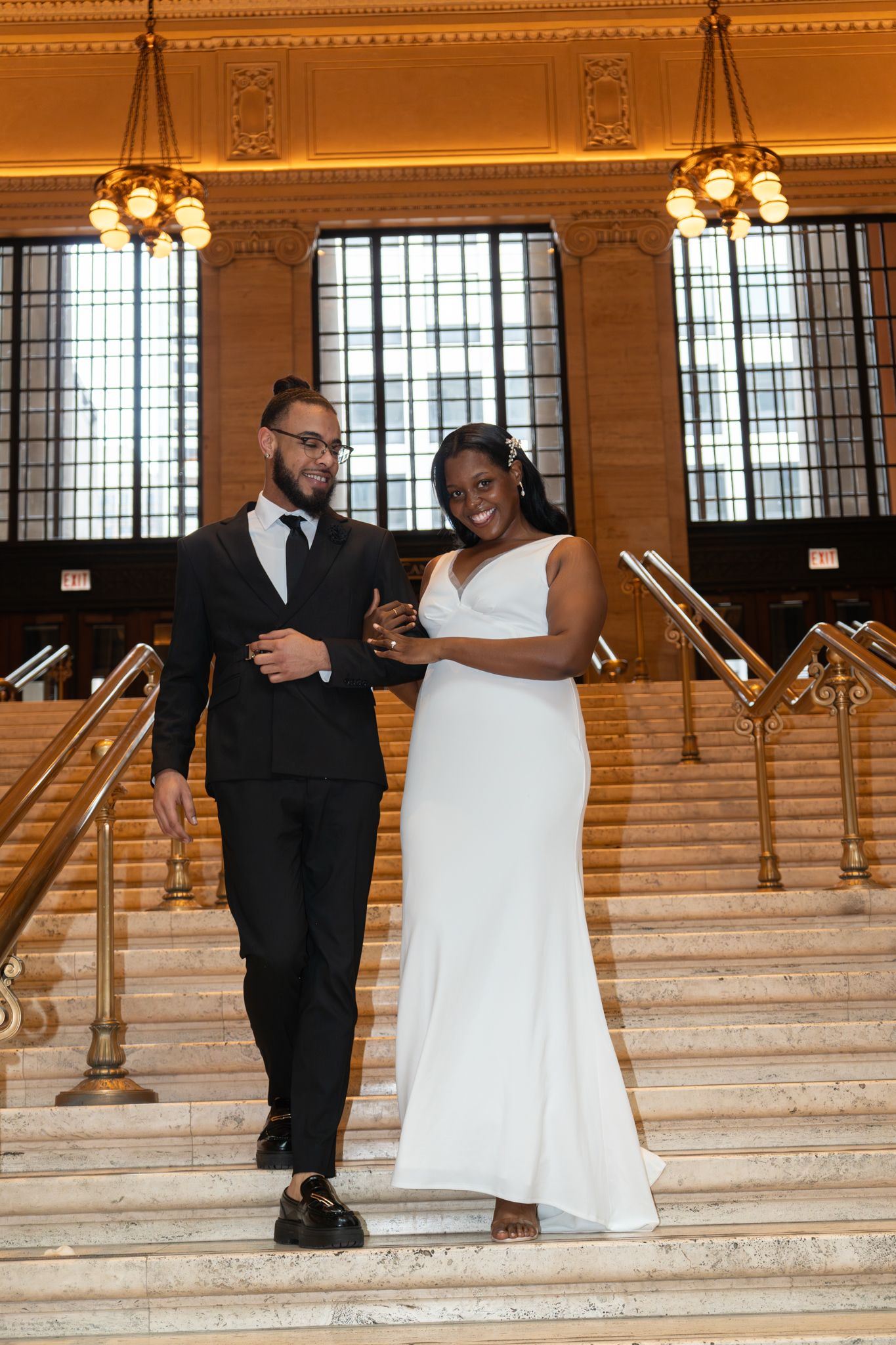 Smiling bride and groom descend grand staircase in stunning historic wedding venue.