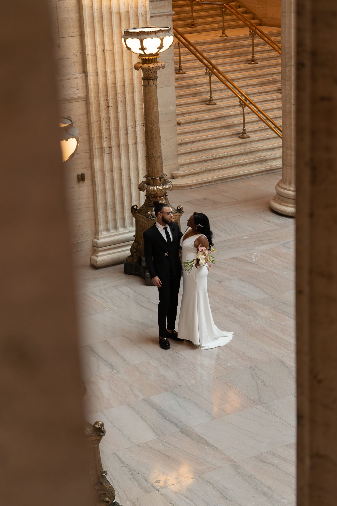 Newlyweds share intimate moment on marble floor of grand columned wedding venue.